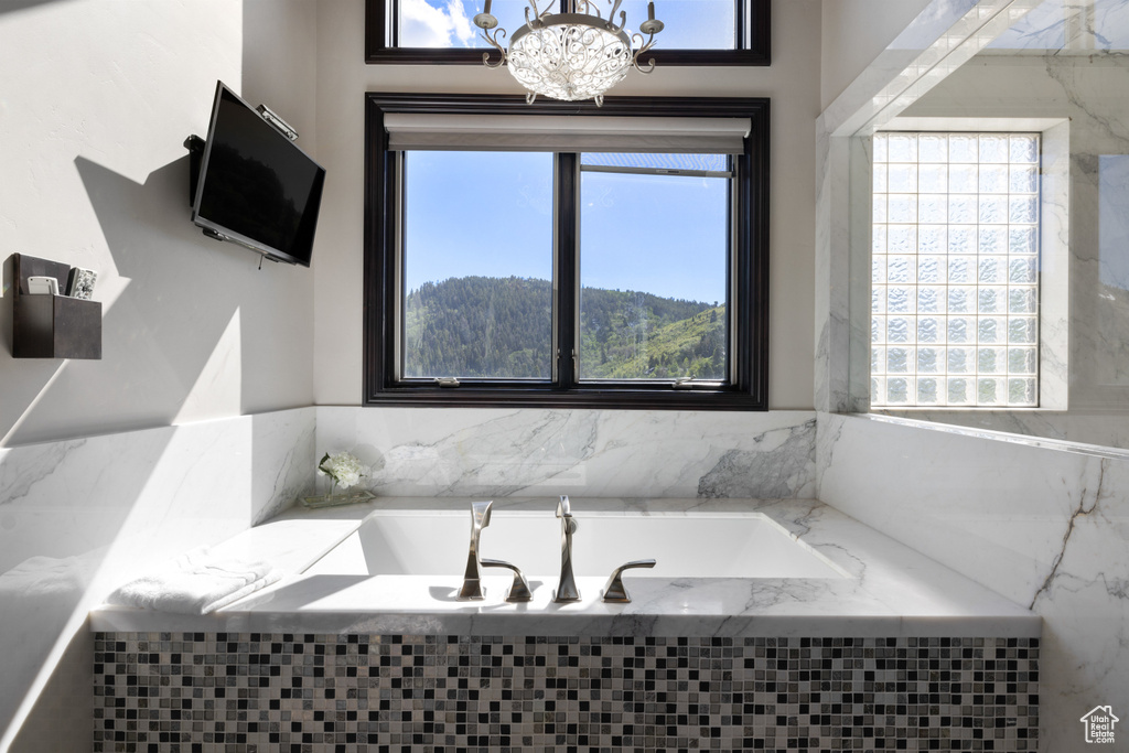 Bathroom with tiled bath, an inviting chandelier, and a wealth of natural light