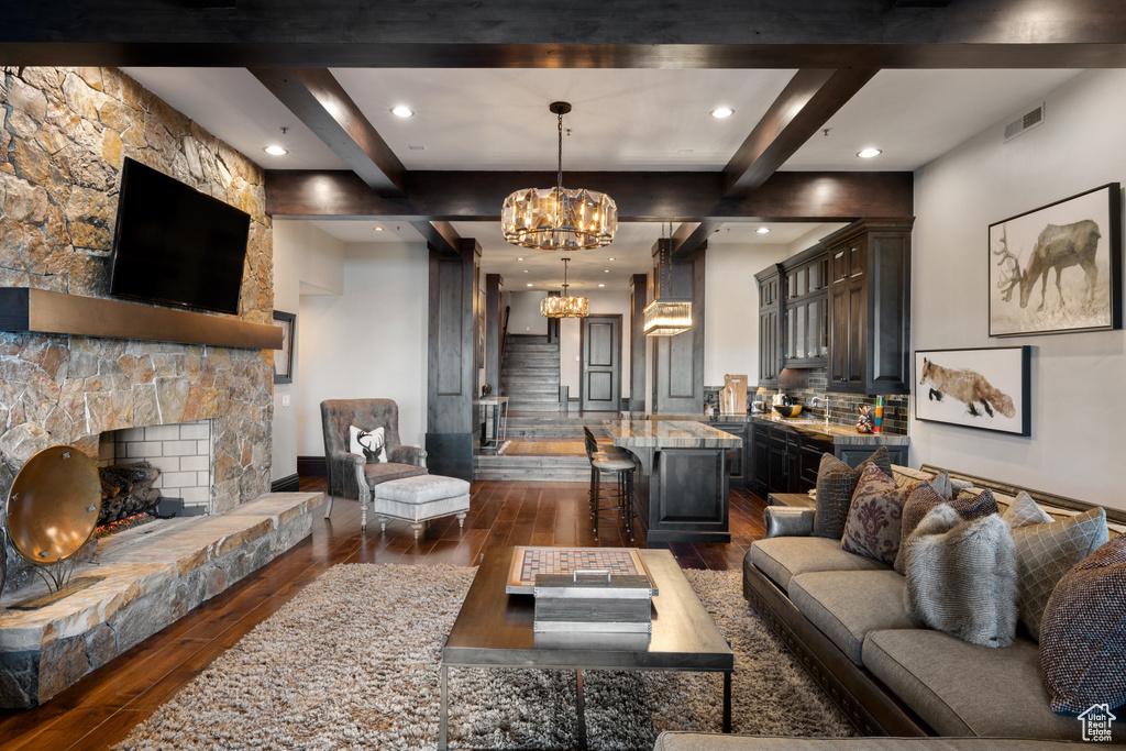 Living room featuring a notable chandelier, a stone fireplace, beamed ceiling, and dark wood-type flooring