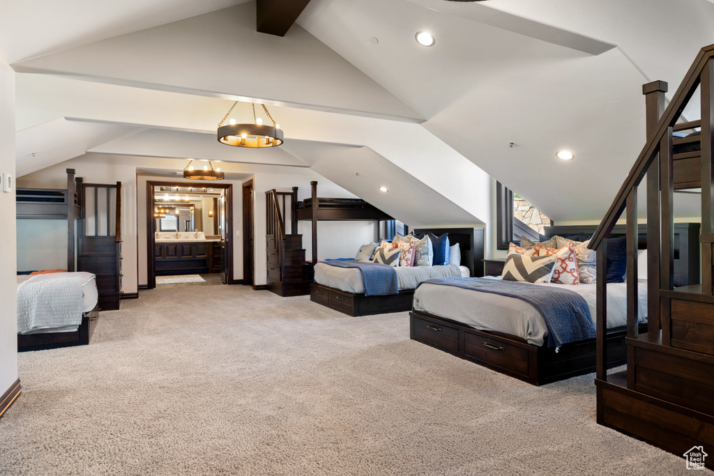 Bedroom featuring ensuite bath, light colored carpet, vaulted ceiling, and a chandelier