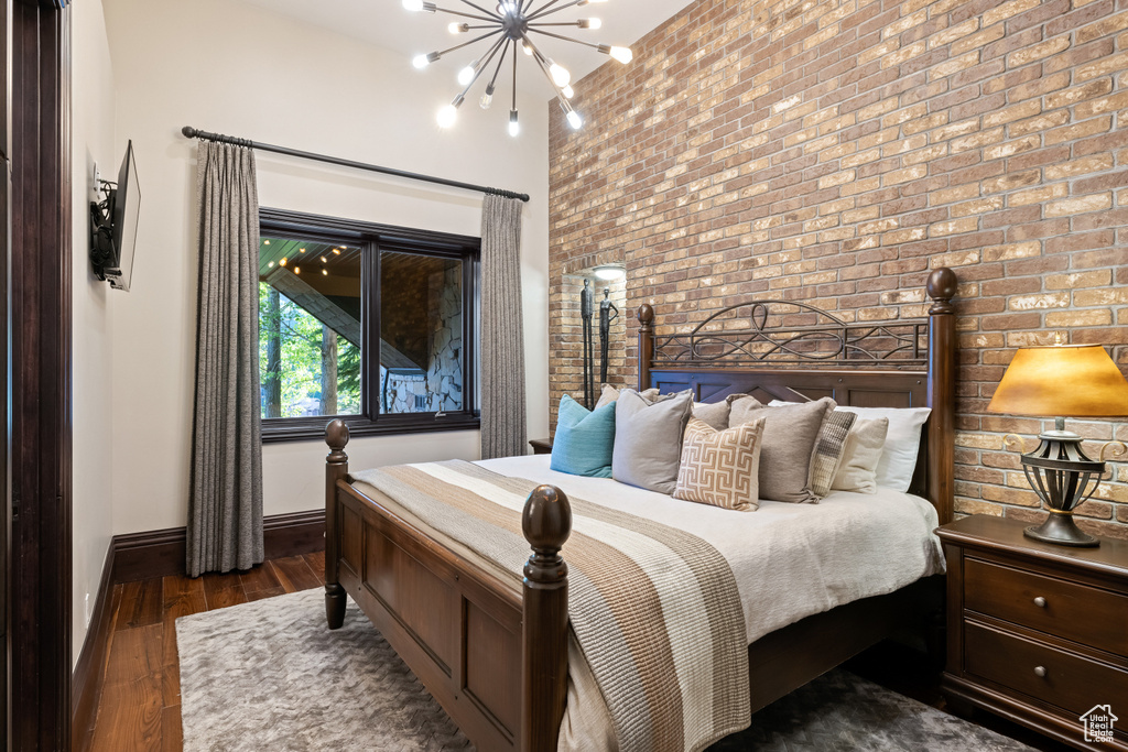 Bedroom with dark wood-type flooring, brick wall, and an inviting chandelier