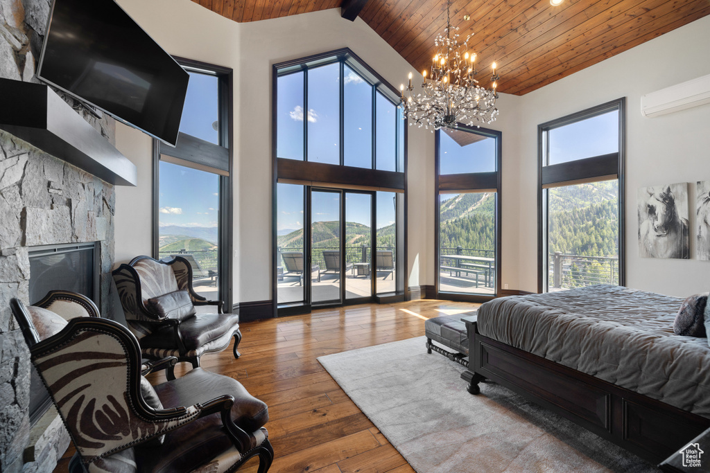 Bedroom featuring a chandelier, high vaulted ceiling, hardwood / wood-style floors, a stone fireplace, and wood ceiling