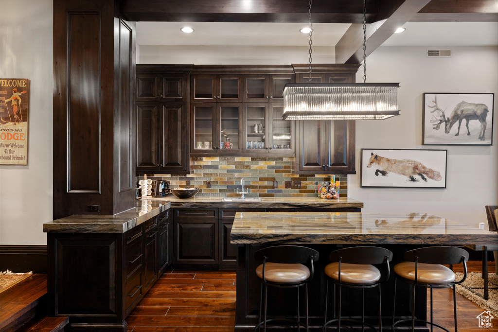 Kitchen featuring a kitchen bar, backsplash, a kitchen island, stone countertops, and dark wood-type flooring