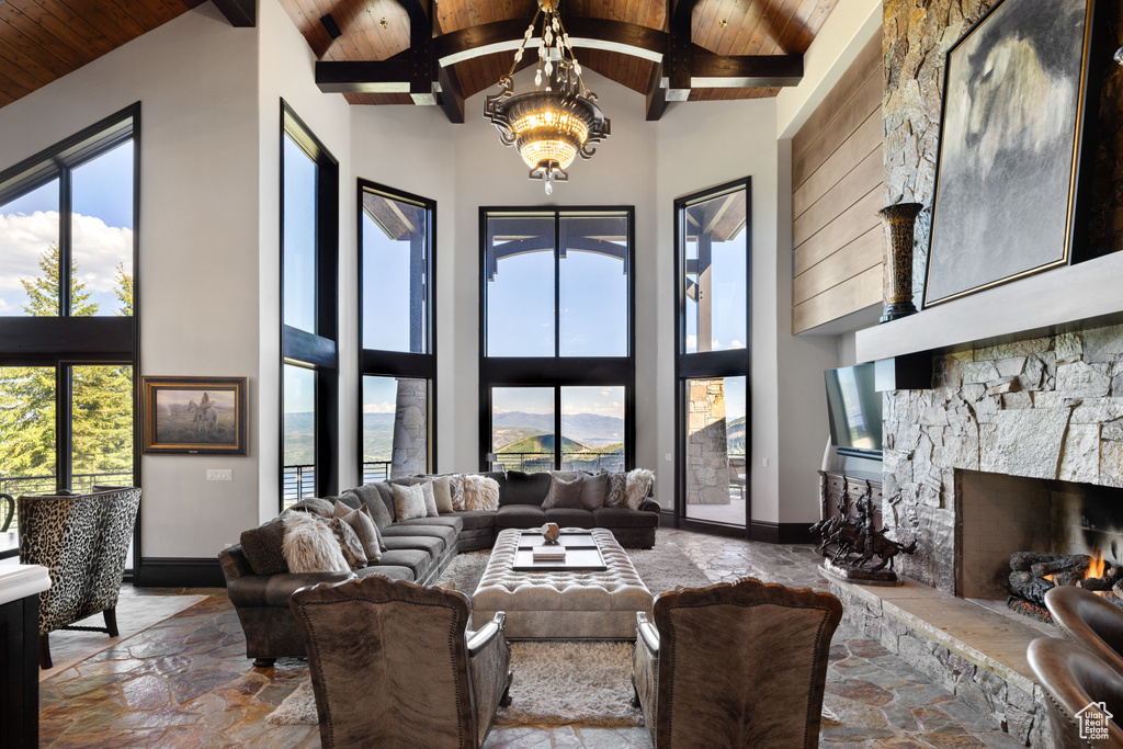 Living room featuring a stone fireplace, a high ceiling, beam ceiling, wooden ceiling, and a notable chandelier