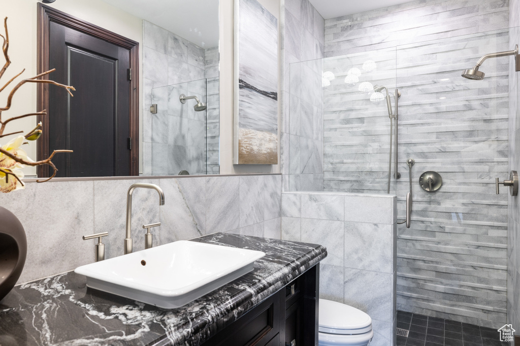 Bathroom with a shower with door, vanity, tile walls, and toilet