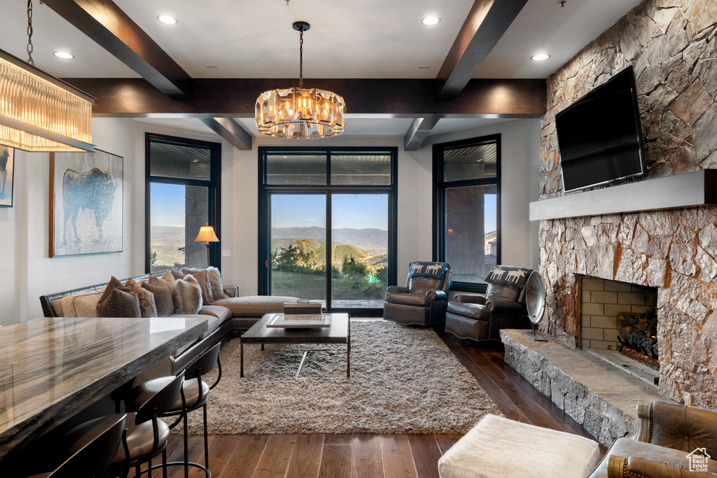 Living room with beam ceiling, a stone fireplace, dark hardwood / wood-style flooring, and a chandelier