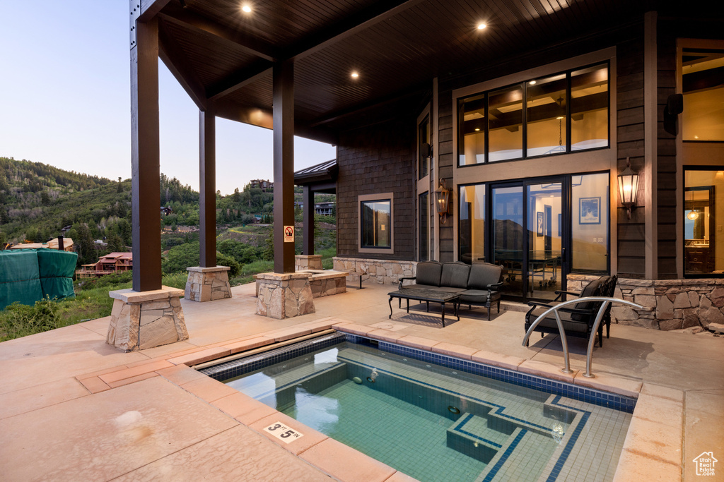 Pool at dusk with outdoor lounge area, a patio, and a mountain view