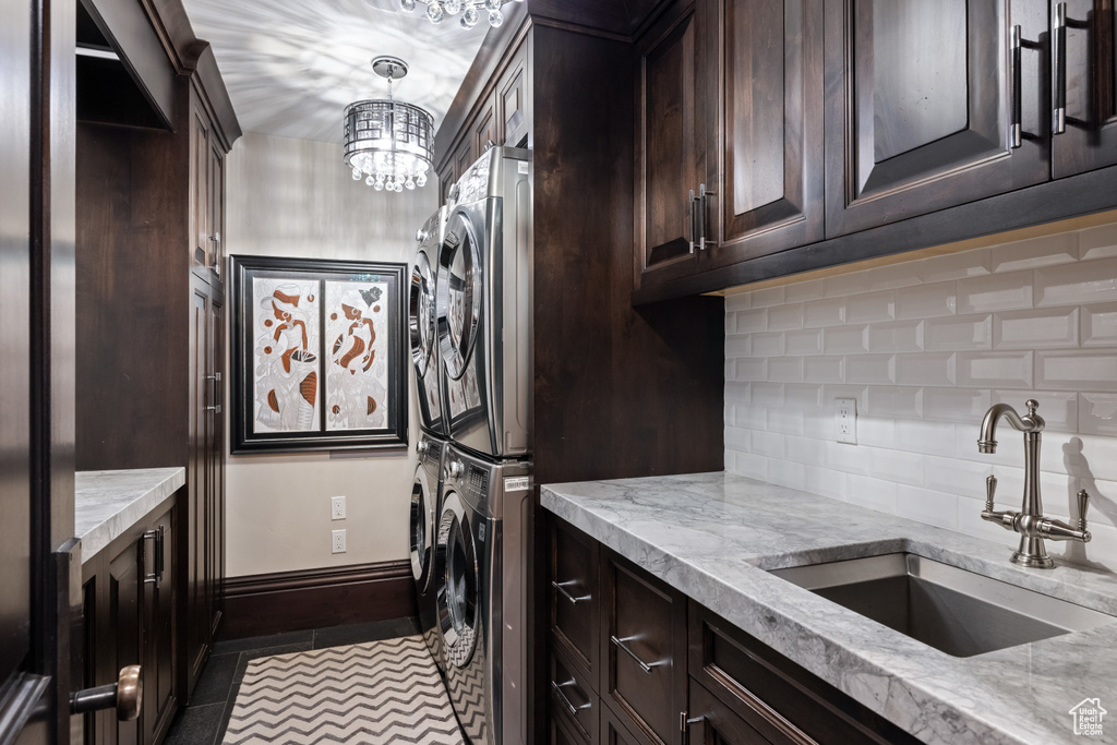 Laundry area featuring an inviting chandelier, sink, tile patterned flooring, cabinets, and stacked washing maching and dryer