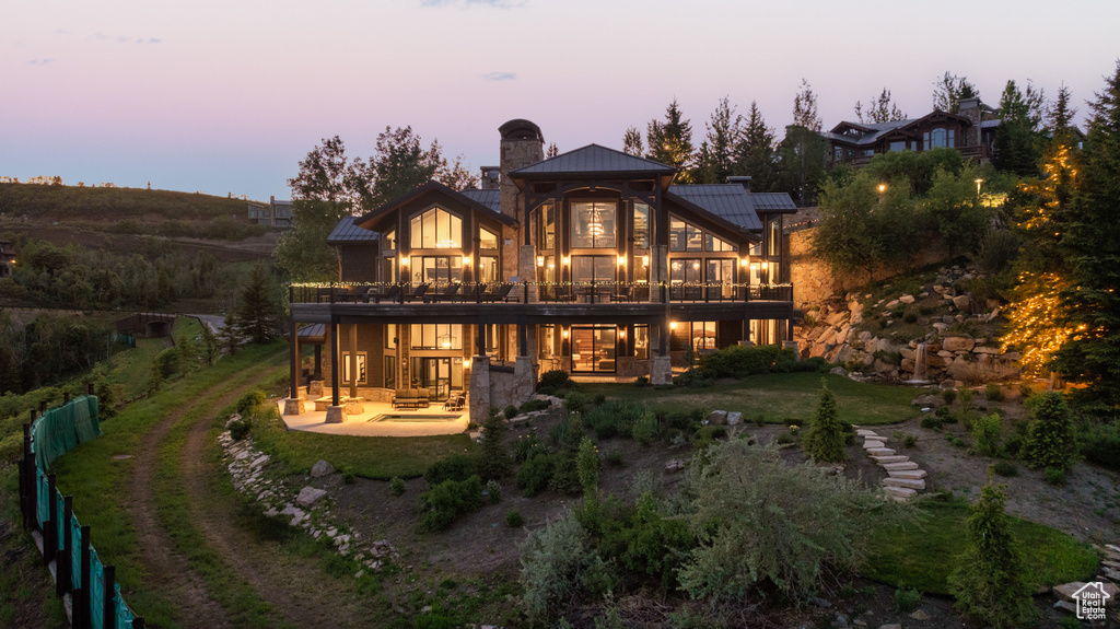 Back house at dusk with a patio and a balcony