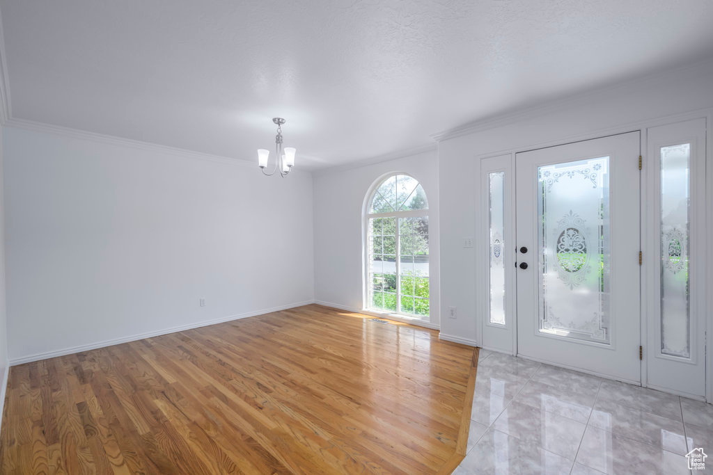 Foyer entrance featuring light hardwood / wood-style floors, a notable chandelier, and crown molding