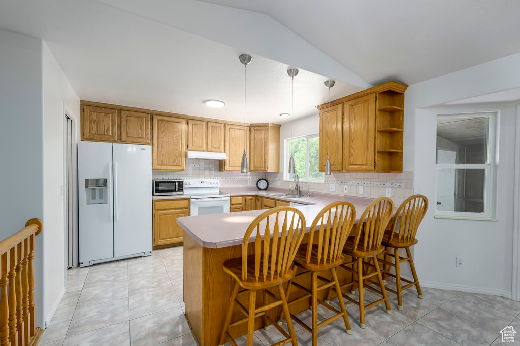 Kitchen with hanging light fixtures, kitchen peninsula, white appliances, light tile patterned floors, and a kitchen breakfast bar