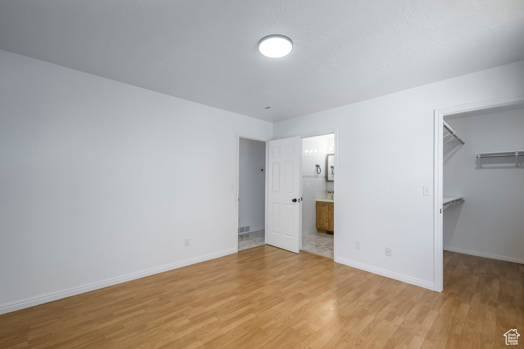 Unfurnished bedroom featuring light hardwood / wood-style floors, a spacious closet, ensuite bath, and a closet