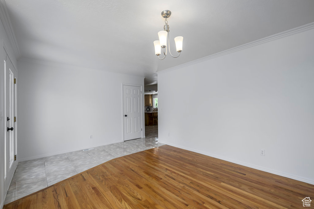 Unfurnished room with light hardwood / wood-style floors, ornamental molding, and an inviting chandelier