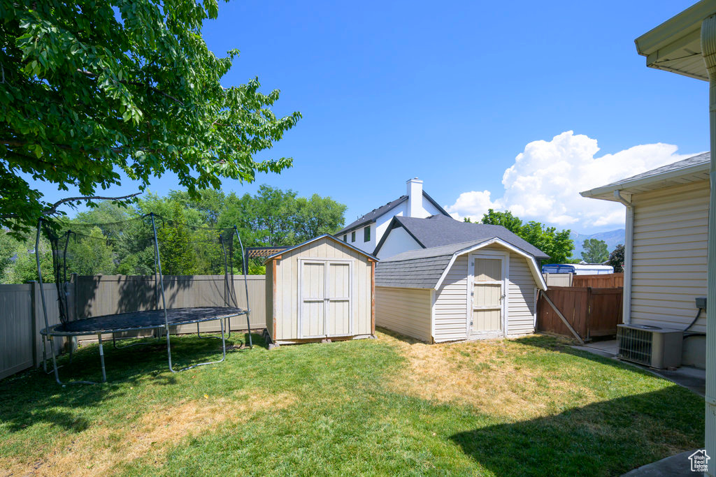 View of yard featuring a trampoline, central AC, and a storage shed