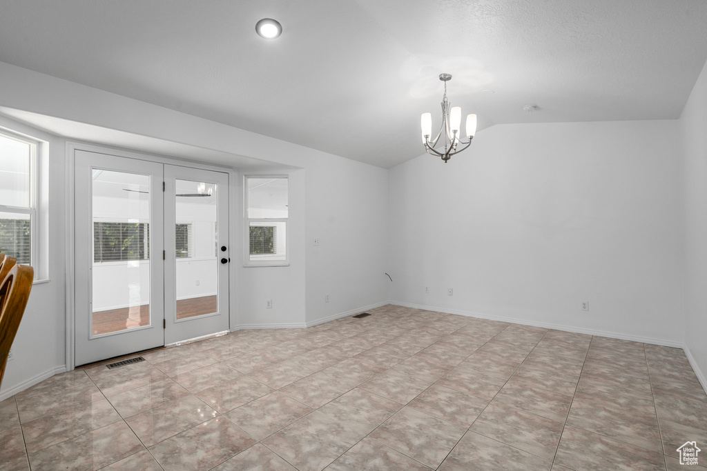 Tiled empty room with a notable chandelier and vaulted ceiling