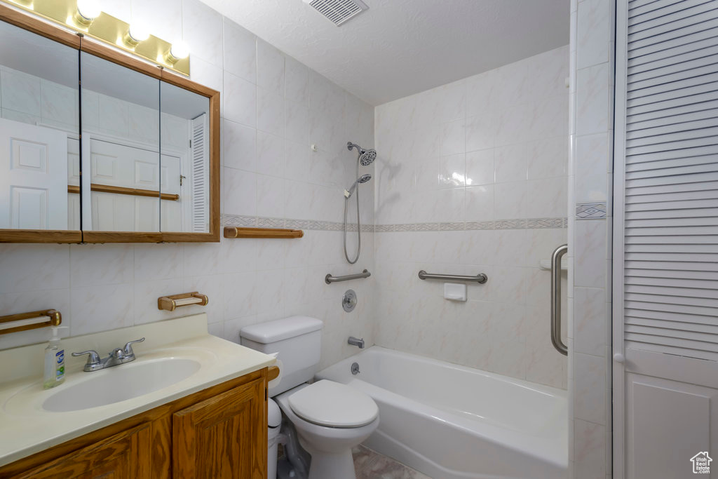 Full bathroom with a textured ceiling, tiled shower / bath combo, toilet, vanity, and tile walls