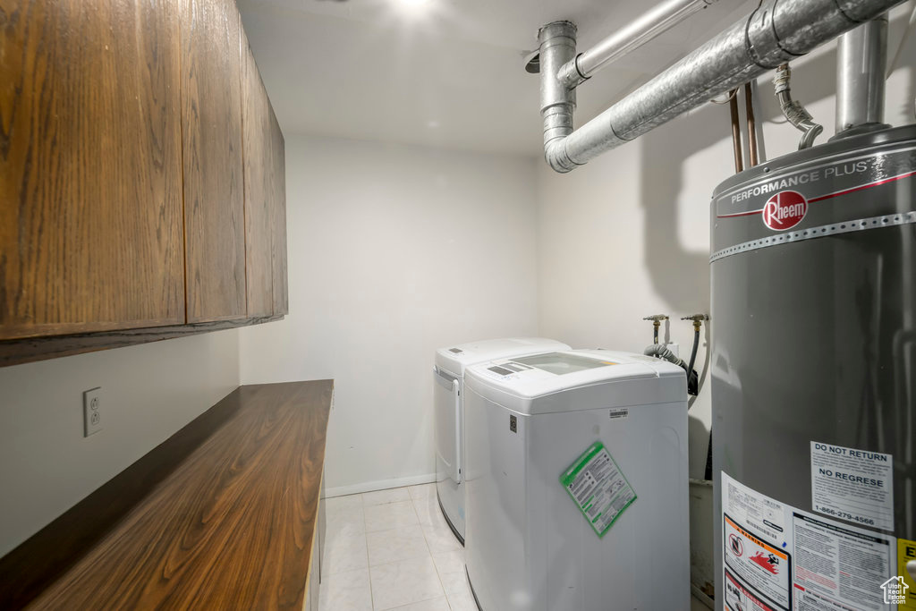 Laundry area featuring washing machine and clothes dryer, water heater, cabinets, and light tile patterned floors