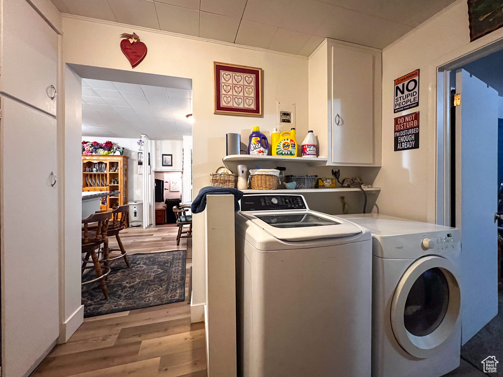 Clothes washing area with separate washer and dryer, light hardwood / wood-style flooring, and cabinets