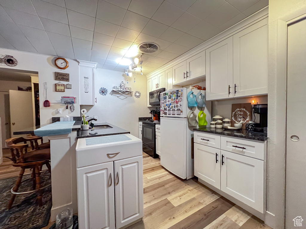 Kitchen featuring white cabinets, light hardwood / wood-style floors, black appliances, and kitchen peninsula