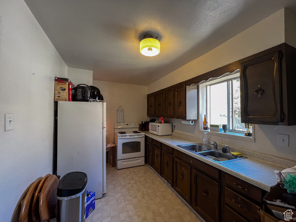 Kitchen with dark brown cabinets, light tile patterned floors, white appliances, and sink