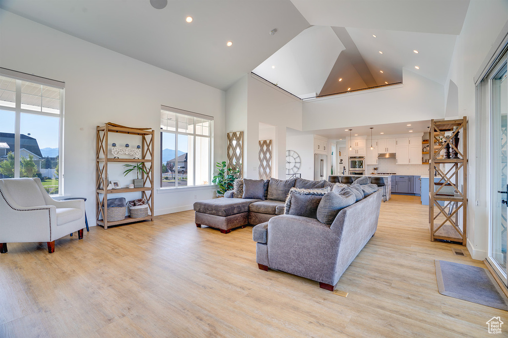 Living room featuring a healthy amount of sunlight, light wood-type flooring, and high vaulted ceiling