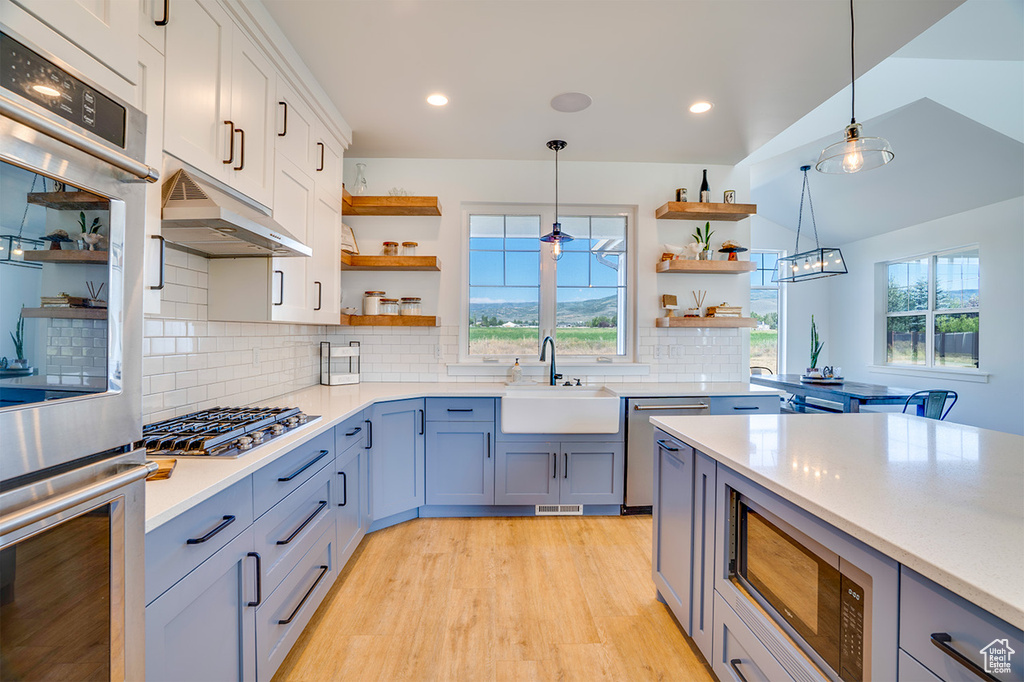 Kitchen with hanging light fixtures, white cabinets, sink, light hardwood / wood-style flooring, and backsplash