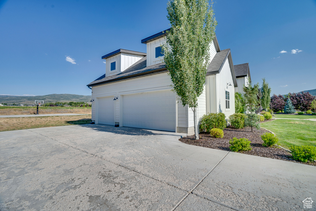 View of property exterior with a mountain view, a garage, and a lawn