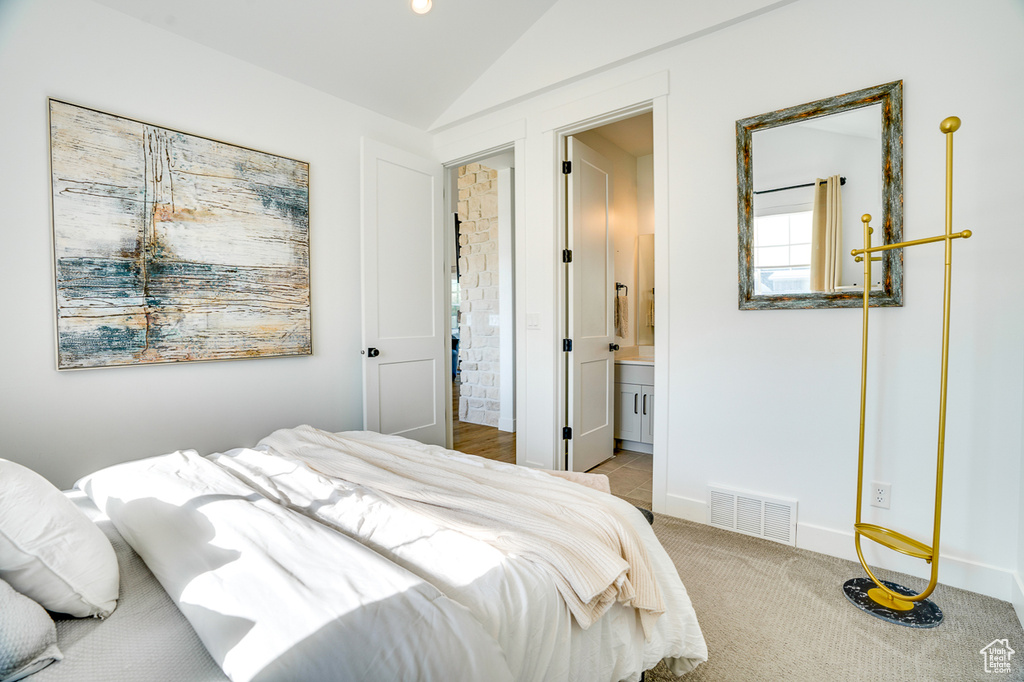 Carpeted bedroom with connected bathroom and vaulted ceiling