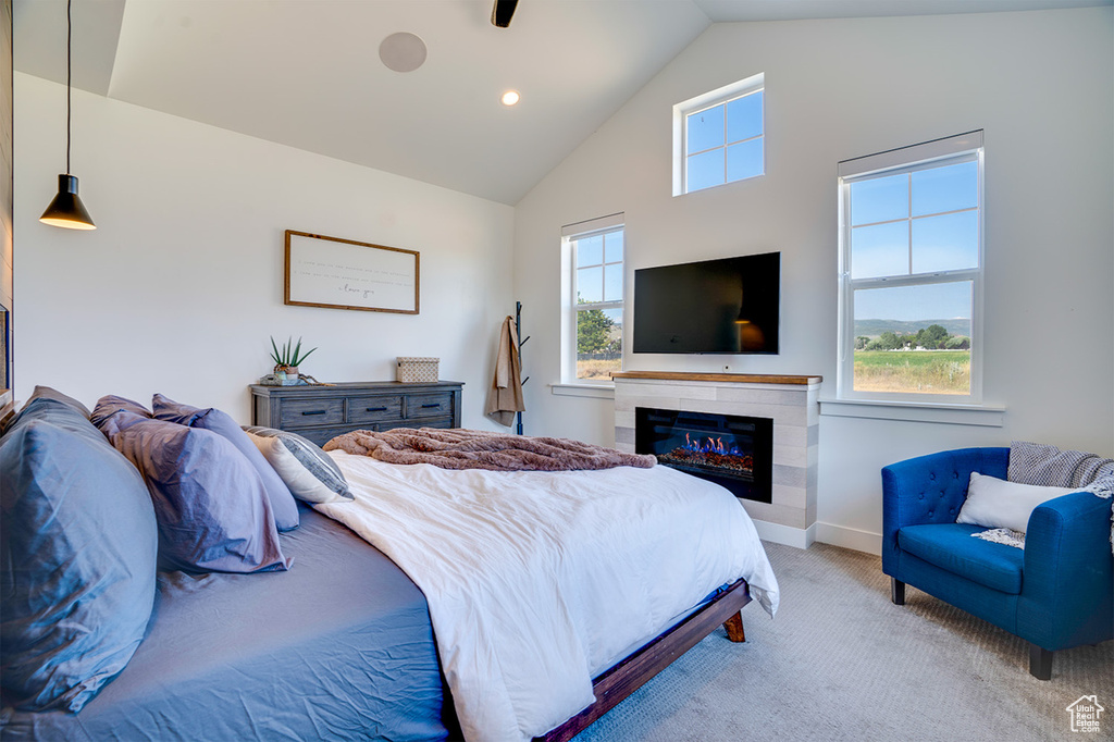 Bedroom with multiple windows, a tiled fireplace, vaulted ceiling, and carpet floors