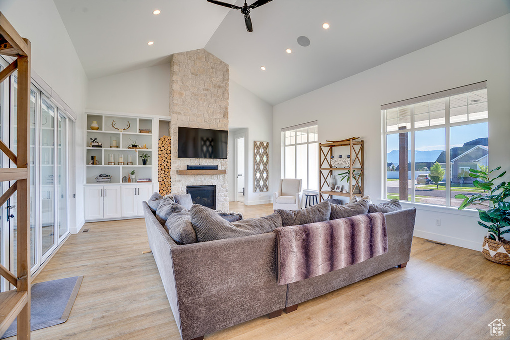 Living room featuring built in features, high vaulted ceiling, a fireplace, and light hardwood / wood-style floors