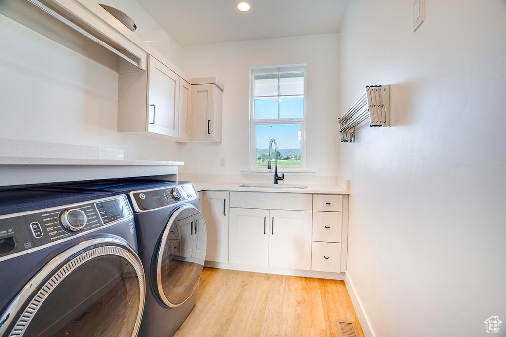 Washroom featuring sink, light wood-type flooring, cabinets, and separate washer and dryer