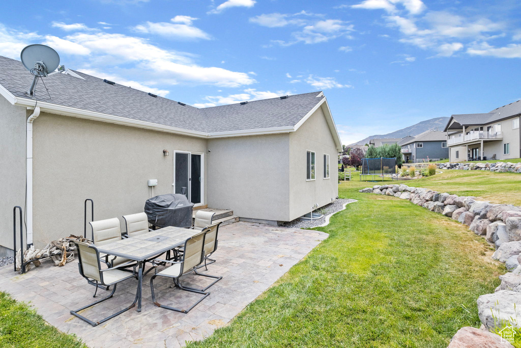 Back of property featuring a patio, a lawn, and a trampoline