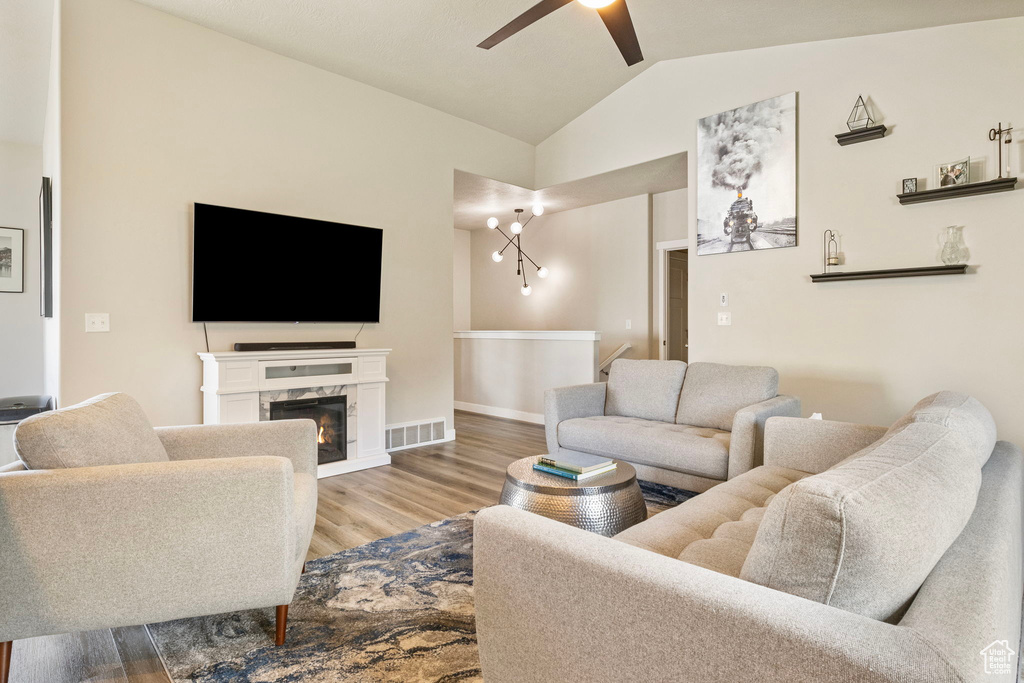 Living room featuring lofted ceiling, light hardwood / wood-style flooring, a premium fireplace, and ceiling fan