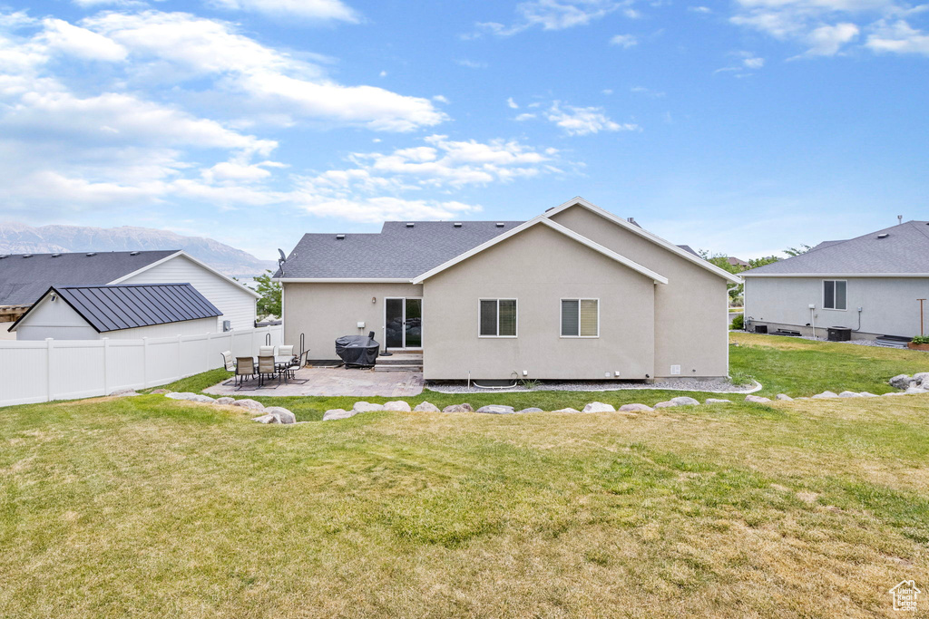 Back of house with a patio, a lawn, and a mountain view