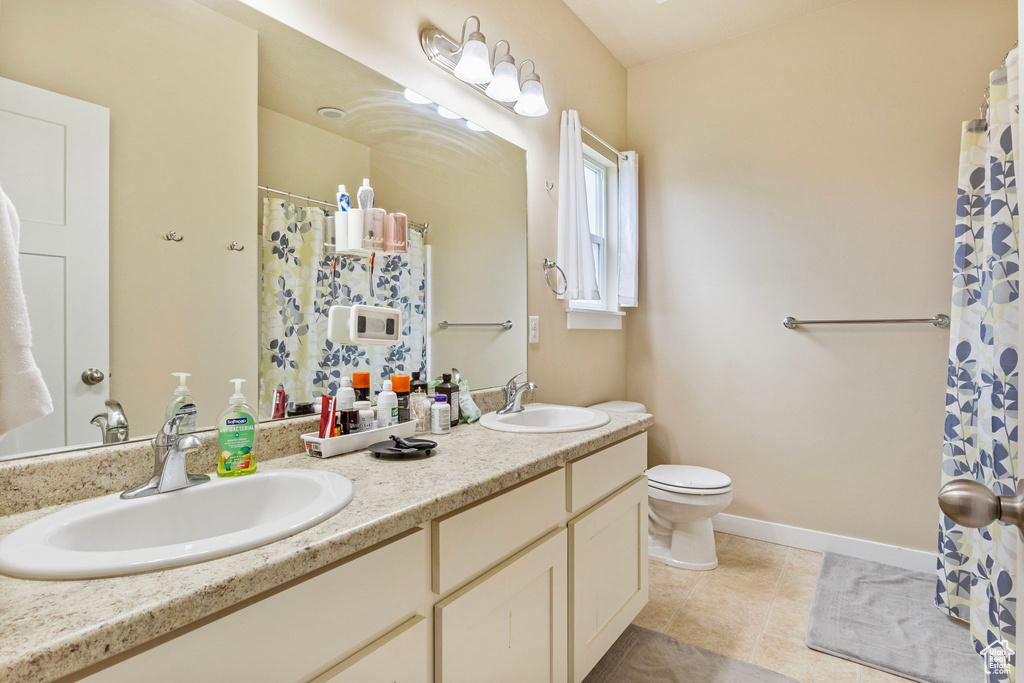 Bathroom with toilet, double sink vanity, and tile patterned flooring