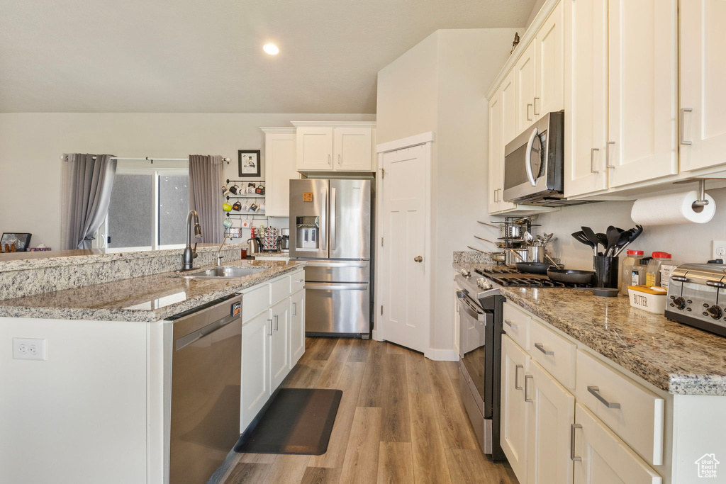 Kitchen with stainless steel appliances, white cabinets, light wood-type flooring, sink, and light stone counters