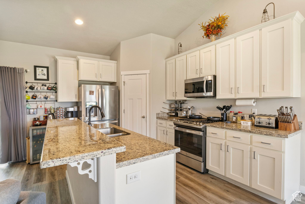 Kitchen featuring appliances with stainless steel finishes, white cabinetry, hardwood / wood-style floors, and sink