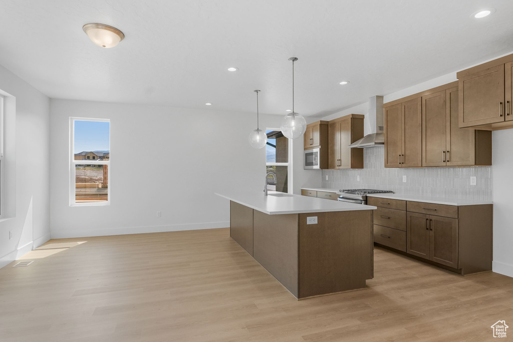 Kitchen featuring light wood-type flooring, tasteful backsplash, a wealth of natural light, and decorative light fixtures