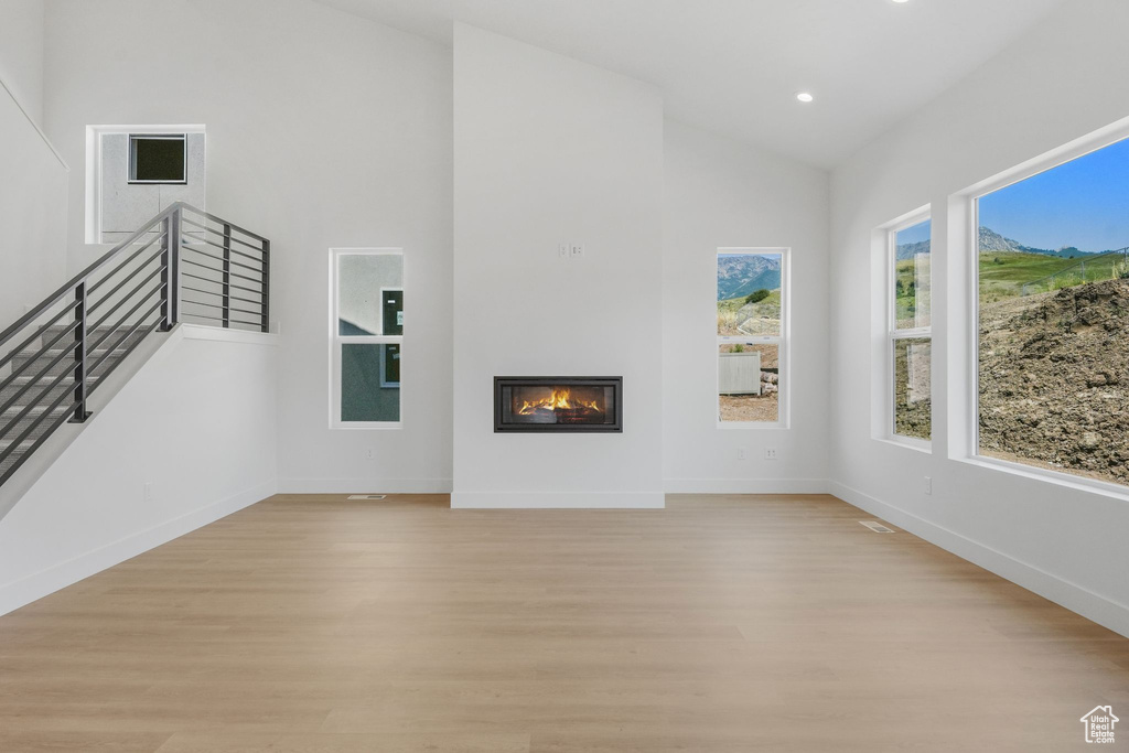 Unfurnished living room featuring plenty of natural light, high vaulted ceiling, and light hardwood / wood-style flooring