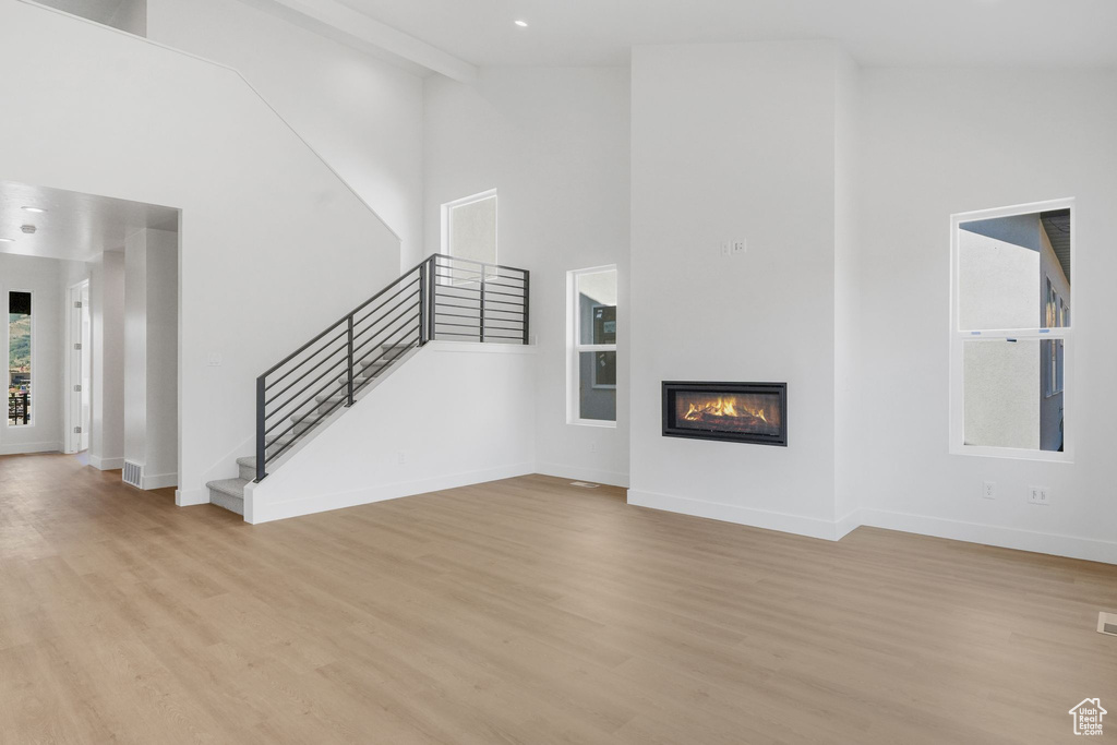 Unfurnished living room with light hardwood / wood-style floors, beam ceiling, and high vaulted ceiling