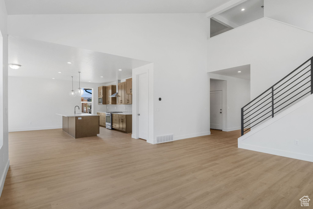 Unfurnished living room featuring light hardwood / wood-style flooring, sink, and high vaulted ceiling