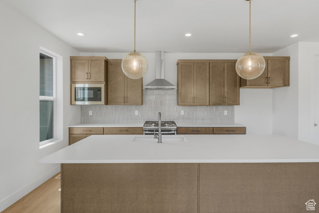 Kitchen with tasteful backsplash, wall chimney range hood, an island with sink, built in microwave, and pendant lighting