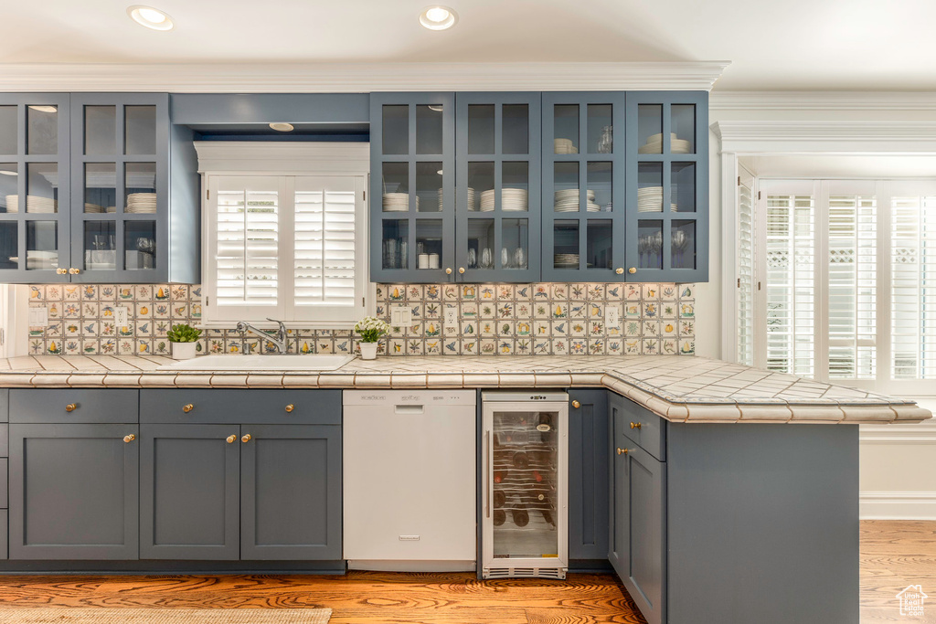 Kitchen featuring backsplash, sink, wine cooler, white dishwasher, and tile countertops