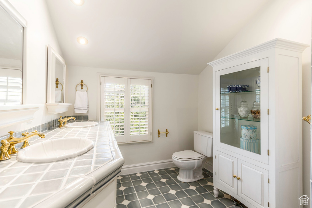 Bathroom featuring toilet, vaulted ceiling, vanity, and tile patterned floors