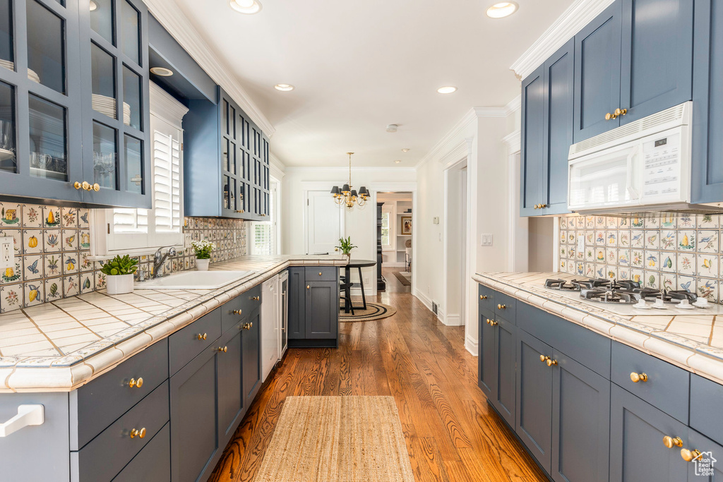 Kitchen with tile counters, dark hardwood / wood-style flooring, tasteful backsplash, hanging light fixtures, and white appliances