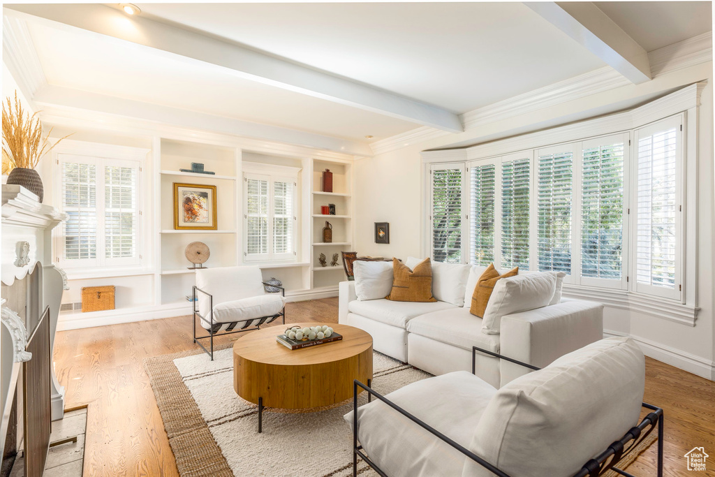 Living room with built in features, beamed ceiling, crown molding, and light hardwood / wood-style flooring