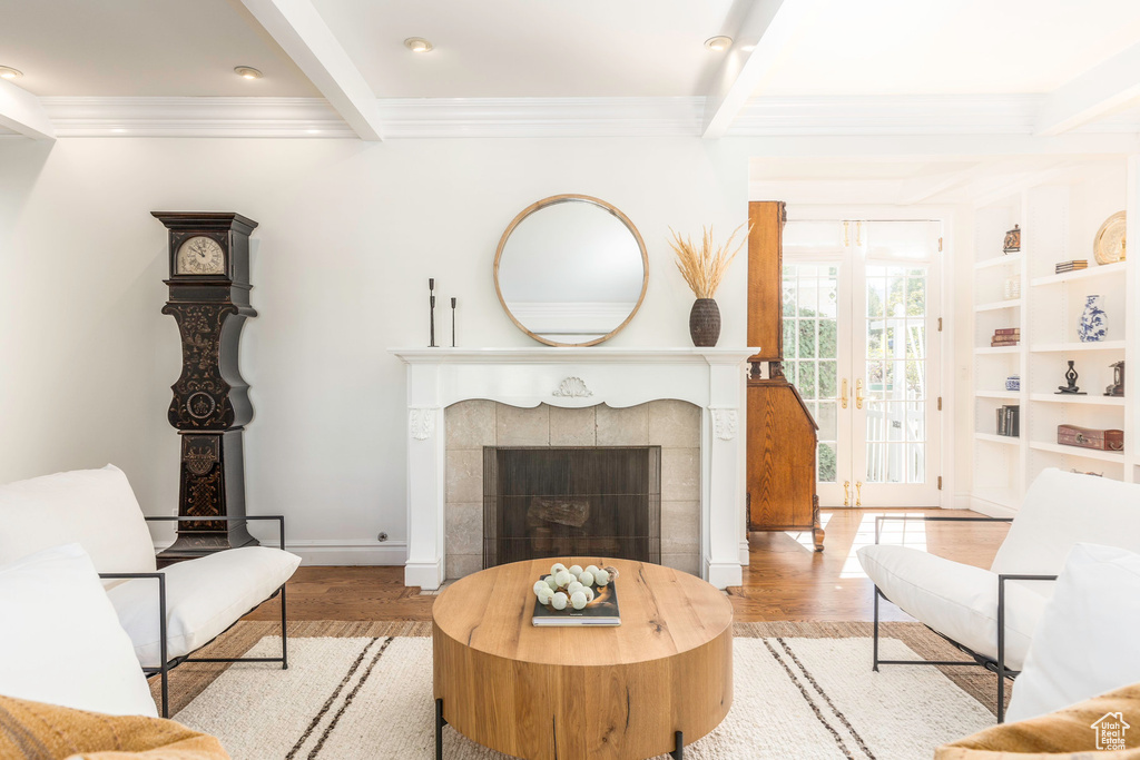 Living area with light wood-type flooring, beam ceiling, crown molding, and a tiled fireplace