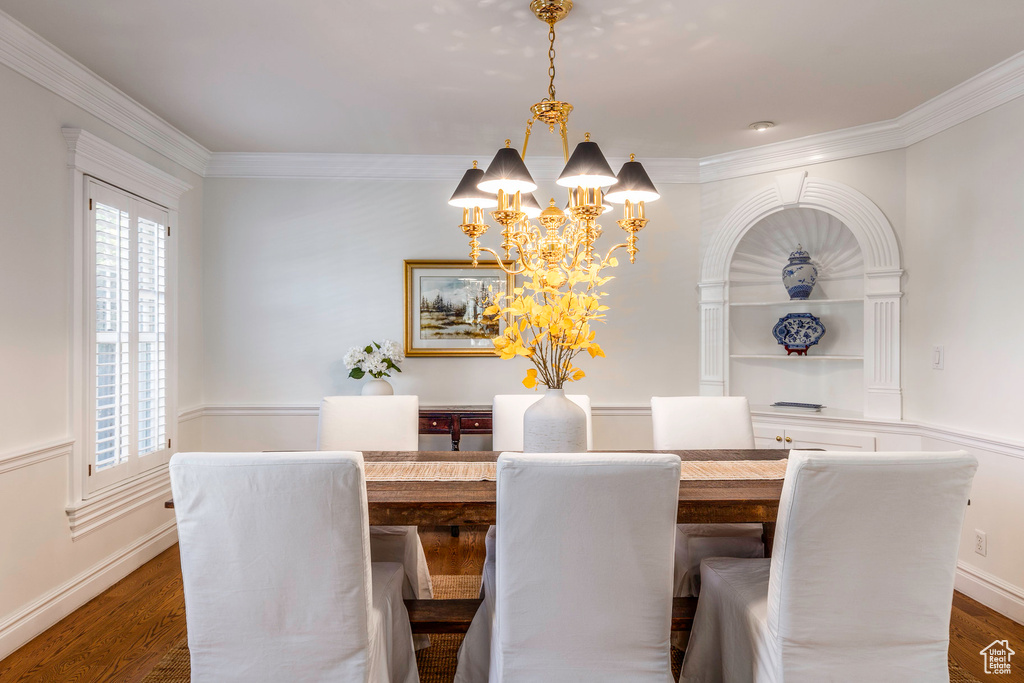 Dining area with a notable chandelier, crown molding, and dark wood-type flooring