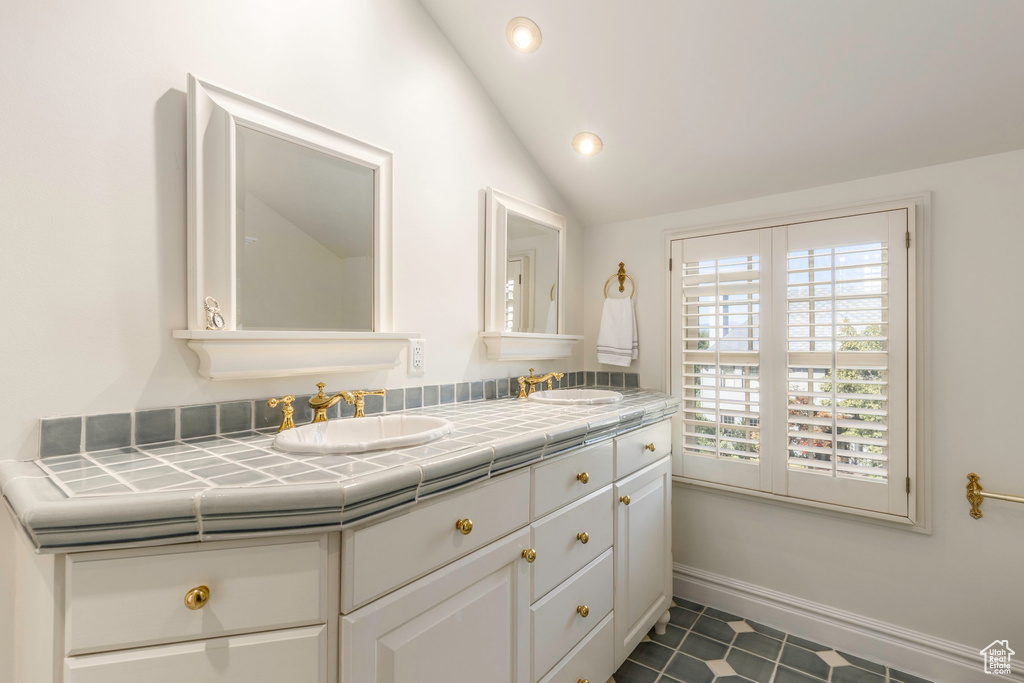 Bathroom featuring a wealth of natural light, vaulted ceiling, tile patterned floors, and vanity