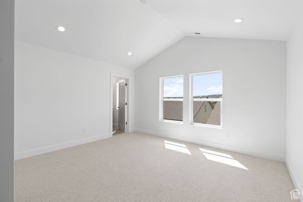 Unfurnished room featuring light colored carpet and vaulted ceiling