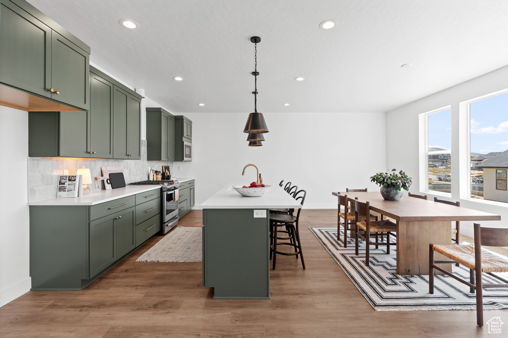 Kitchen with tasteful backsplash, green cabinetry, stove, and light hardwood / wood-style floors